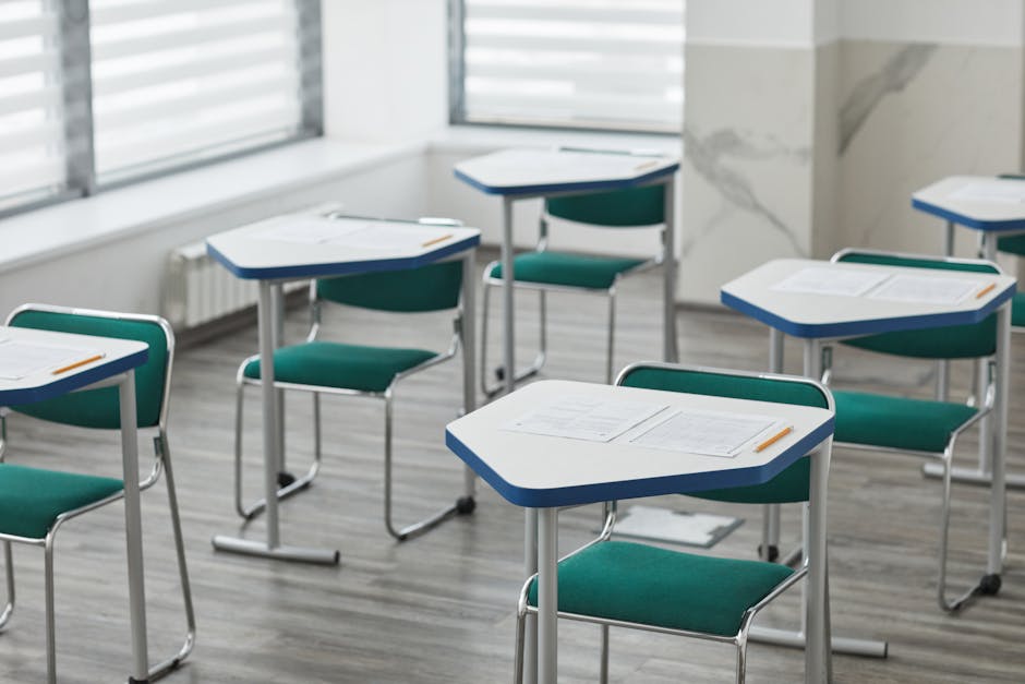 An empty classroom with arranged desks, exam papers, and pencils ready for students